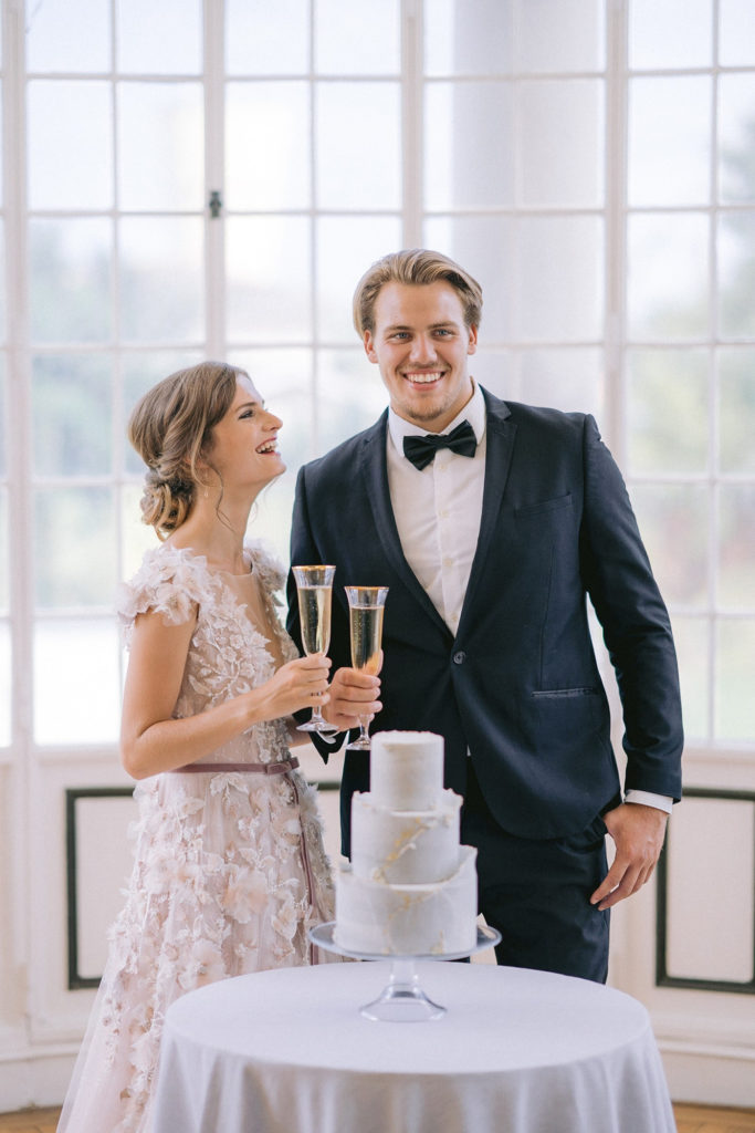 couple de mariés buvant du champagne devant leur wedding cake mis en scène par la wedding planner Amélie Pichon Weddings