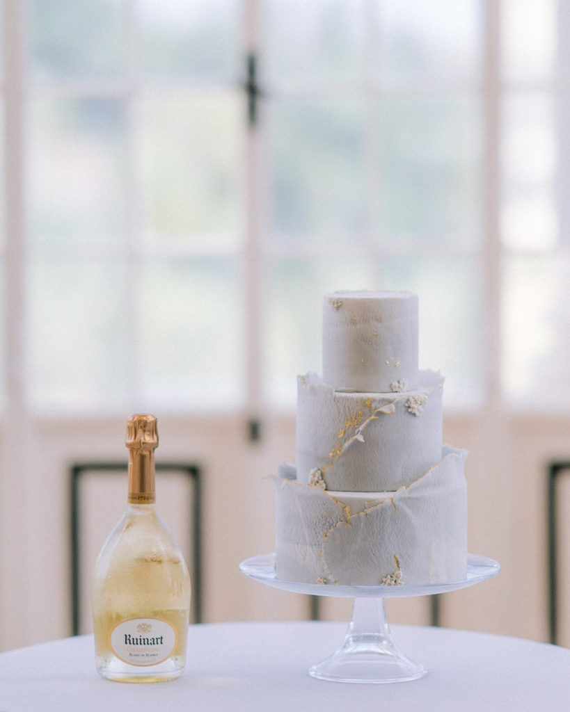 Wedding Cake et bouteille de champagne ruinart posés sur une table devant une fenêtre mis en scène par la wedding planner Amélie Pichon Weddings