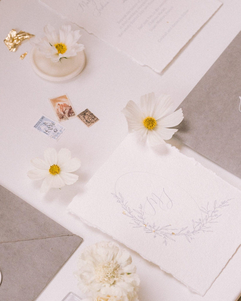Flatlay papeterie de mariage avec des timbres et des fleurs mis en scène par la wedding planner Amélie Pichon Weddings