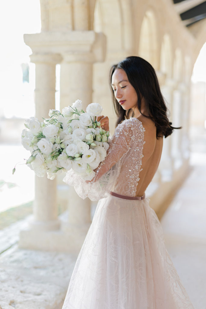 Mariée en robe regardant son bouquet fleurs blanches mis en scène par la wedding planner Amélie Pichon Weddings